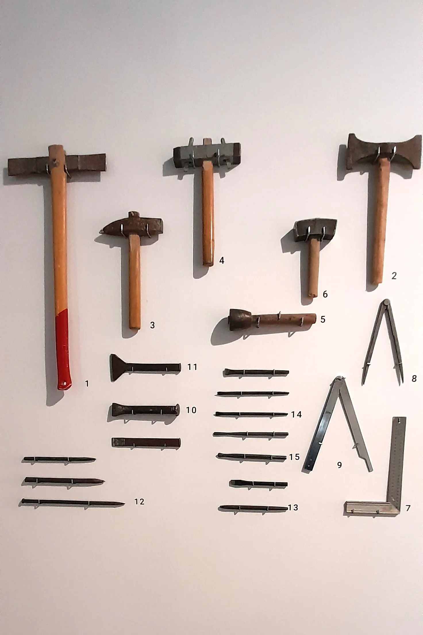 Portrait-format reference photograph of stonemasonry hammers, chisels, points, measuring tools and compasses, stone type not applicable, shown at hand-tool scale.