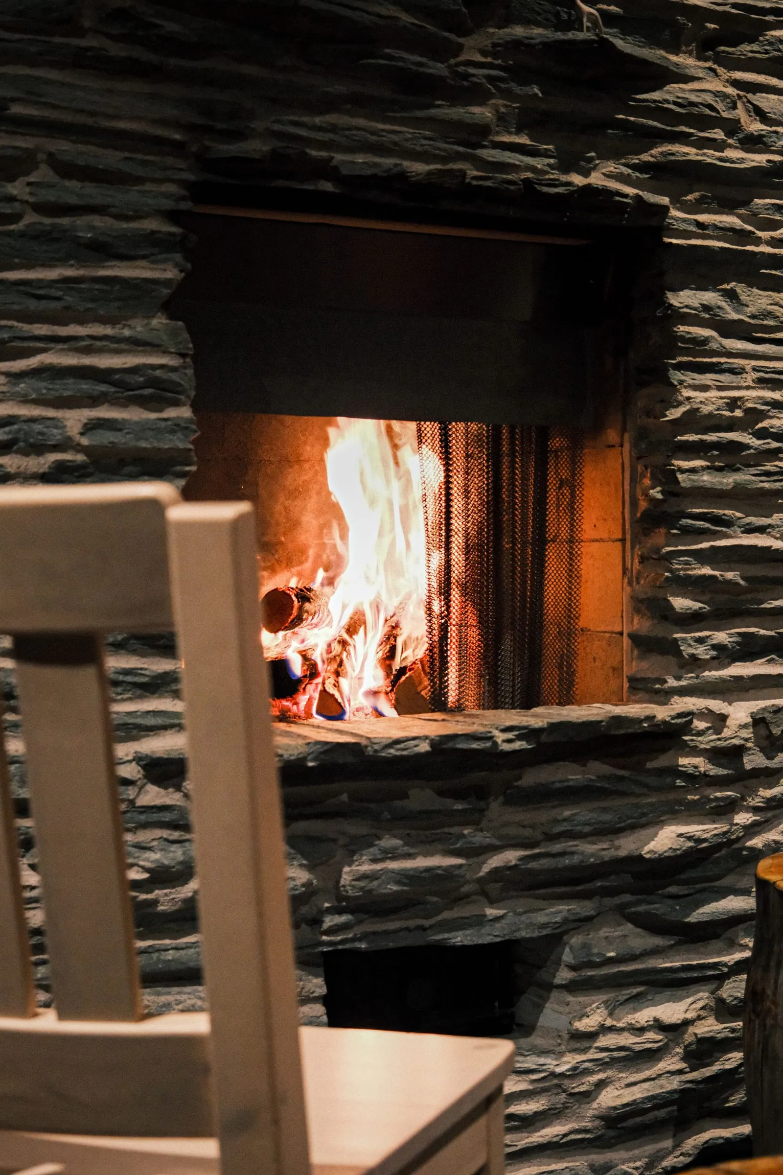 Room-scale stock photograph of a rustic stacked-stone fireplace with a burning fire, exact stone type unverified.